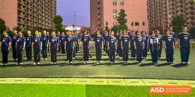 A large group of students from The First High School of Changsha, Hunan standing in formation outside on a sports ground in front of a school building.