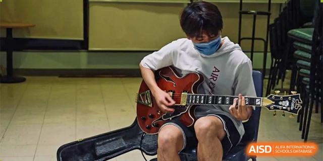 A student from The First High School of Changsha, Hunan playing an electric guitar, sitting next to an open guitar case.