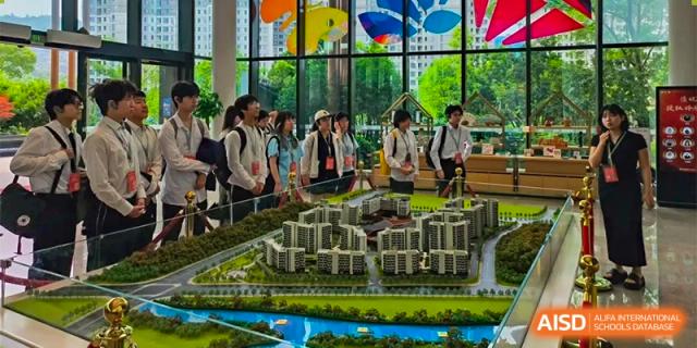 Students from The First High School of Changsha, Hunan gathered around a detailed architectural model of a town or campus, looking at it with interest.