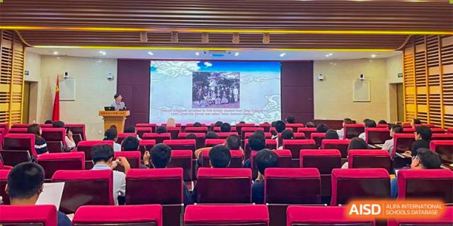 Students and faculty from The First High School of Changsha, Hunan seated in a large auditorium, watching a historical presentation or photo on a big screen.