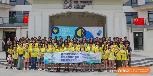 A large group of Vindu-Charlie Lakefield College students and staff posing with a banner for the "American Youth Exchange Program" in front of a school building.