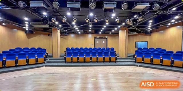 An empty auditorium or presentation room at Vindu-Charlie Lakefield College featuring wooden floors and a row of blue and yellow seats in the foreground.