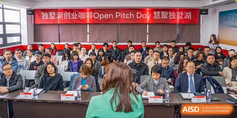 A conference or event at Vindu-Charlie Lakefield College with students and attendees seated, looking toward a presentation under an "Open Pitch Day" banner.