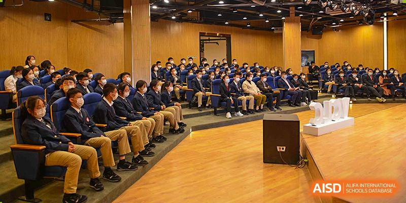 A large group of Vindu-Charlie Lakefield College students wearing dark blue uniforms seated attentively in a modern lecture hall or auditorium.