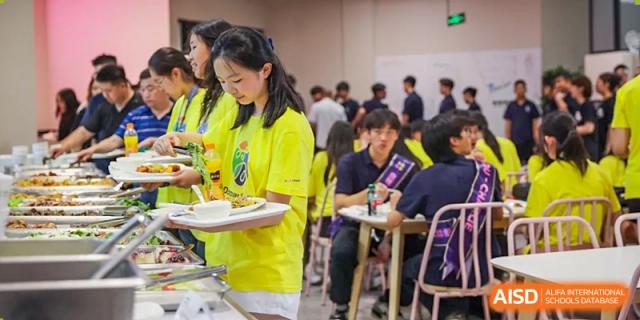 A female student carries a tray of food past other students in the busy dining area or cafeteria at Vindu-Charlie Lakefield College.