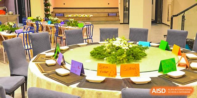 A close-up of a formal dining table with a lazy Susan, a green centerpiece, and name cards for guests at Vindu-Charlie Lakefield College.