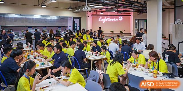 A large group of students in yellow shirts sit at tables and eat a meal in the dining hall at Vindu-Charlie Lakefield College.