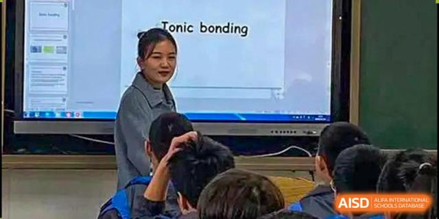 A female teacher from The High School Attached to Hunan Normal University lecturing on "Ionic bonding" using an interactive whiteboard while students listen in a classroom.