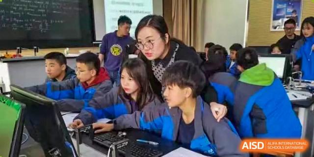 A teacher from The High School Attached to Hunan Normal University providing one-on-one guidance to students working on a computer during a technology or project-based learning session.
