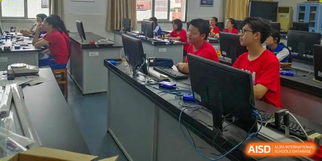 Students from The High School Attached to Hunan Normal University working at desktop computers in a dedicated computer lab or media room.