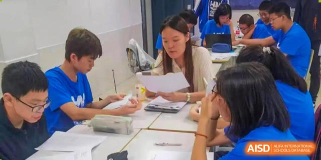 A female student from The High School Attached to Hunan Normal University reviewing papers with a small group of classmates at a desk.
