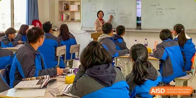 A teacher from The High School Attached to Hunan Normal University lecturing the class from the front of the room, pointing at material written on a whiteboard.