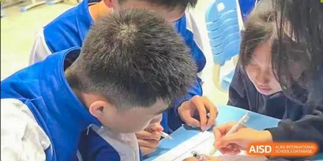 A close-up shot of a student from The High School Attached to Hunan Normal University in a blue uniform concentrating on writing or working on a task at their desk.