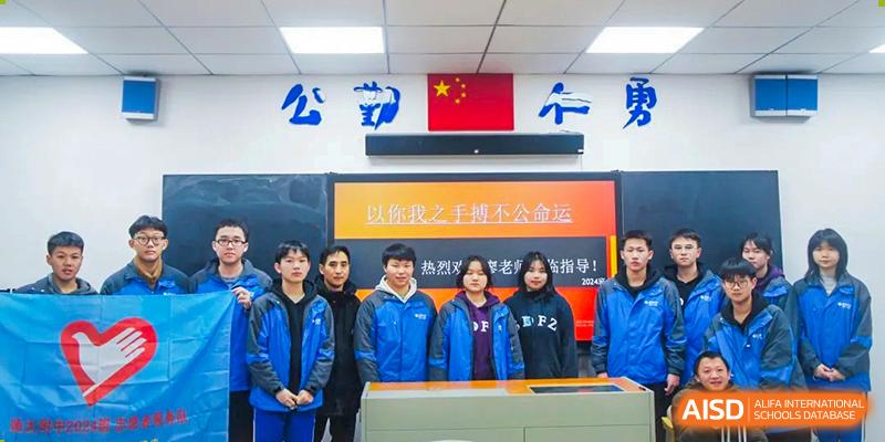 A group of students from The High School Attached to Hunan Normal University posing in front of a wall display with the Chinese flag and motivational text, likely in a classroom or school setting.