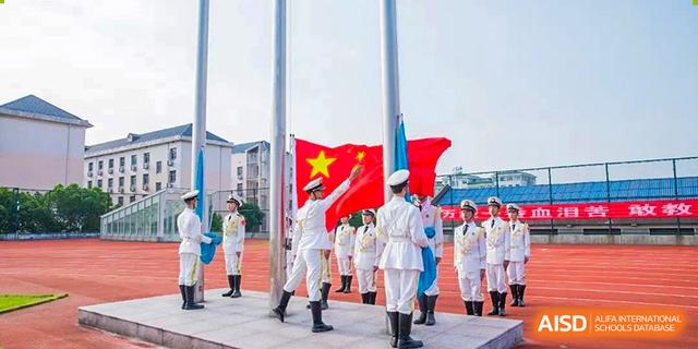 A uniformed honor guard from The High School Attached to Hunan Normal University participating in an outdoor flag-raising ceremony, featuring the Chinese and other flags.