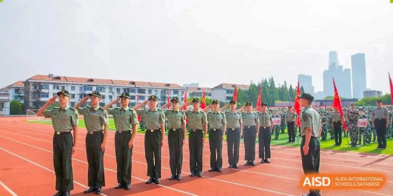 A line of students from The High School Attached to Hunan Normal University in military-style uniform standing in formation on a track and giving a salute, likely during a drill or ceremony.