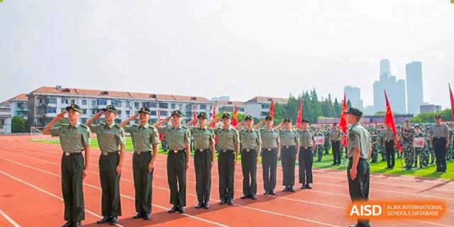 A line of students from The High School Attached to Hunan Normal University in military-style uniform standing in formation on a track and giving a salute, likely during a drill or ceremony.
