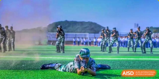 A student from The High School Attached to Hunan Normal University in camouflage uniform doing a prone position drill on a green field during military training.