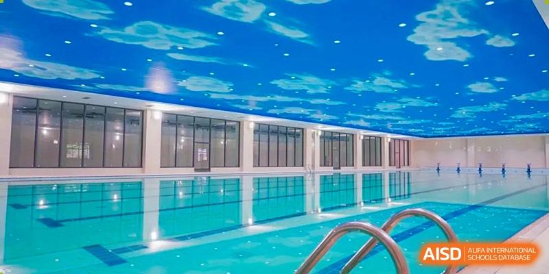 The modern indoor swimming pool at The High School Attached to Hunan Normal University, featuring bright blue water and a unique ceiling painted with clouds.