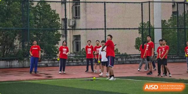 A small group of students from The High School Attached to Hunan Normal University participating in a sports or team-building game on a green field outside a school building.