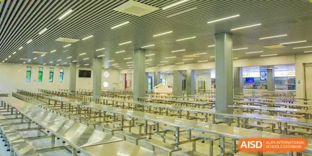 The interior of the large, modern, and well-lit dining hall or cafeteria at The High School Attached to Hunan Normal University, featuring rows of metal tables and chairs.