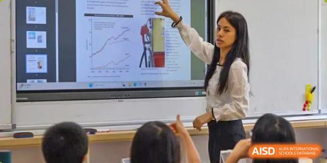 A Wenzhou Union International School (WUIS) teacher pointing to and explaining a graph on a large digital screen to a student.