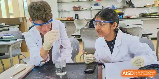 Two Wenzhou Union International School (WUIS) students in safety goggles and a lab coat working on a science experiment in a laboratory.