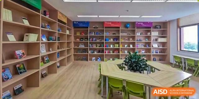 A bright and tidy reading room or library at Wenzhou Union International School (WUIS) with bookshelves, tables, and green chairs.