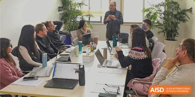 Wenzhou Union International School (WUIS) students and staff collaborating around a modern white table with laptops and supplies in an office or workspace.