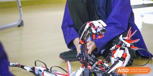 A close-up of a student in a blue uniform assembling a complex robotics project with black and red components at Wenzhou Union International School (WUIS).