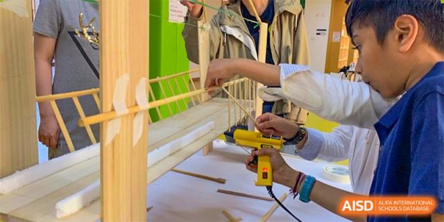 A close-up of an adult and a student at Wenzhou Union International School (WUIS) using a power tool to build a small wooden structure.