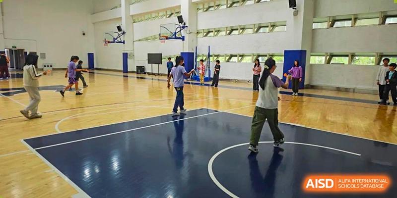 Wenzhou Union International School (WUIS) students and a teacher walking on the glossy, indoor basketball court in the gymnasium.