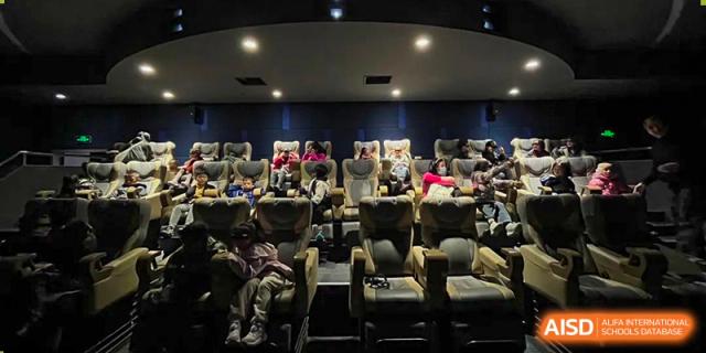 Wenzhou Union International School (WUIS) students relaxing in reclining seats in the darkened school movie theater or auditorium.
