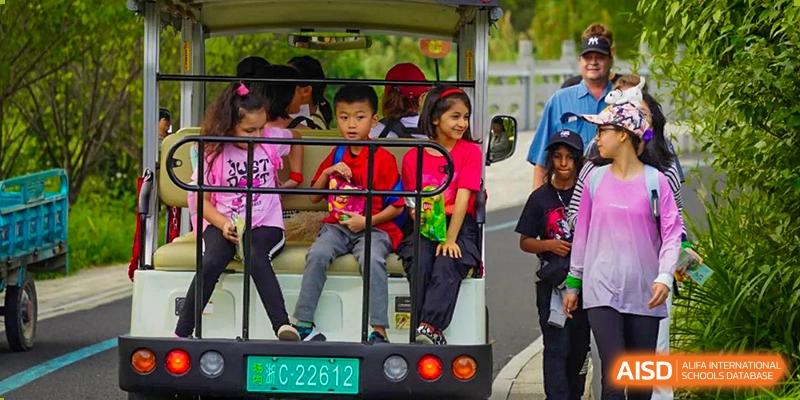 A group of cheerful Wenzhou Union International School (WUIS) students riding in a small, covered electric vehicle on the school campus.