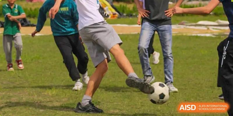A close-up of a Wenzhou Union International School (WUIS) student kicking a soccer ball on an outdoor field during a game.