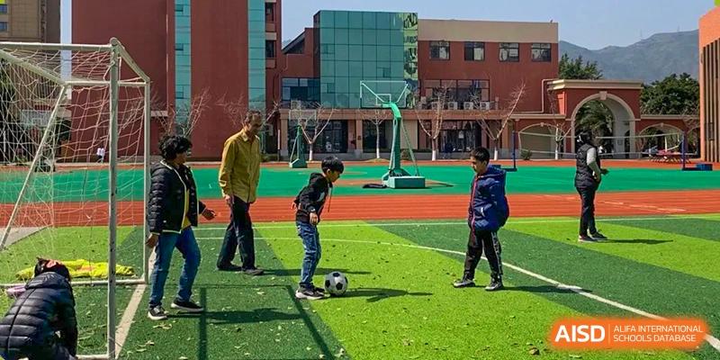 Older Wenzhou Union International School (WUIS) students playing soccer on a turf field near the school's modern main building.