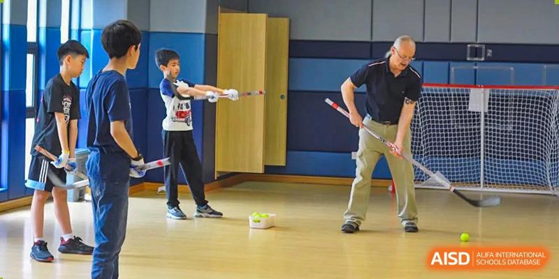 A Wenzhou Union International School (WUIS) student practicing floor hockey, dribbling a ball past an adult in the gymnasium.
