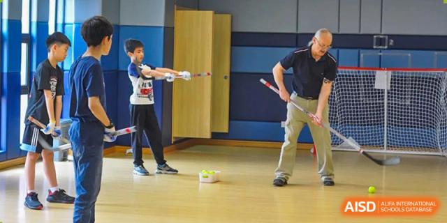 A Wenzhou Union International School (WUIS) student practicing floor hockey, dribbling a ball past an adult in the gymnasium.