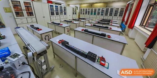 CNUH-GA Curriculum Partnership Program An empty classroom or laboratory with rows of long, grey tables. Scientific or technical equipment, including black and red blocks, is lined up on the tables.