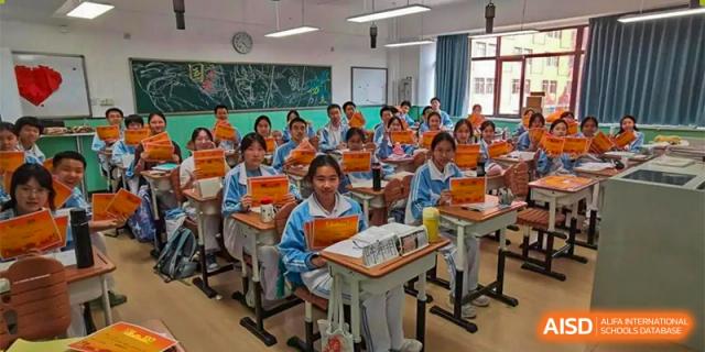 CNUH-GA Curriculum Partnership Program Students in a classroom, wearing light blue uniforms, smiling and holding certificates or small awards while sitting at their desks.