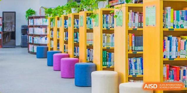 CNUH-GA Curriculum Partnership Program A colorful indoor reading or study area with bright pink, purple, and white round stools in front of tall wooden bookshelves.