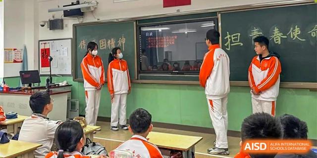 CNUH-GA Curriculum Partnership Program Students in red and white uniforms stand in a classroom near a chalkboard, with one student sitting in the foreground.