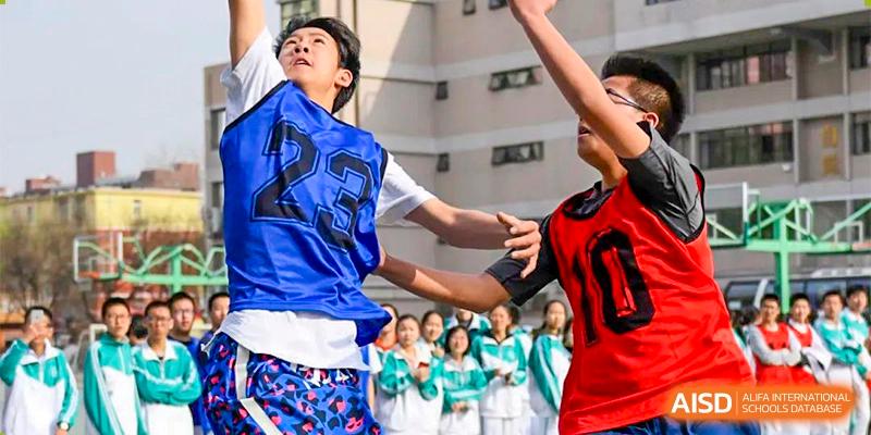 A student from the CNUH-GA Curriculum Partnership Program jumping for a basketball during an outdoor game, with classmates watching below.