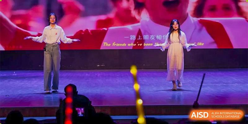A close-up of a stage and screen displaying lyrics or a message in both Chinese and English for a performance at the CNUH-GA Curriculum Partnership Program event.