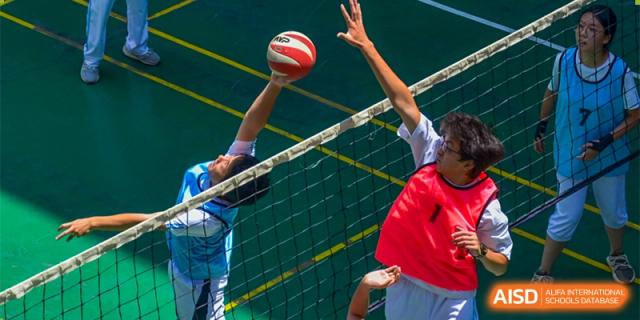 A volleyball player from the CNUH-GA Curriculum Partnership Program spiking the ball over the net during an intense game.