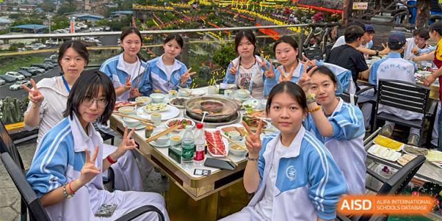 CNUH-GA Curriculum Partnership Program Students sitting around a table with a hot pot meal, with one student in the foreground smiling and making a peace sign.