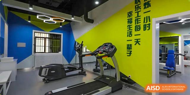 CNUH-GA Curriculum Partnership Program An indoor gym area with a black treadmill against a vibrant yellow and blue wall. Chinese characters are visible on the yellow wall.