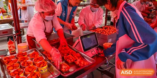 CNUH-GA Curriculum Partnership Program A person in a white and red apron cutting pieces of raw meat on a metal tray under bright red lighting.