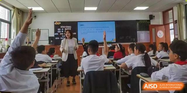 A teacher at Yancheng Foreign Language School interacting with students in the classroom, with a student raising their hand.