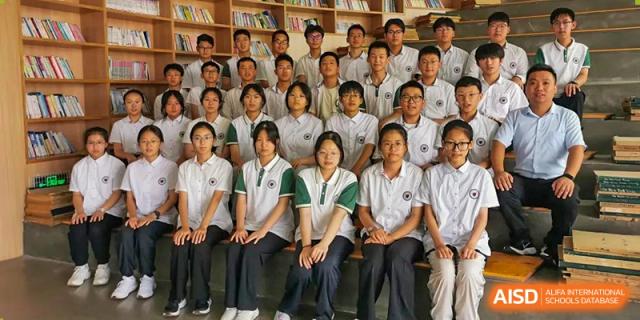 A group portrait of happy Yancheng Foreign Language School students, some wearing green-trimmed uniforms, in a library or media center.